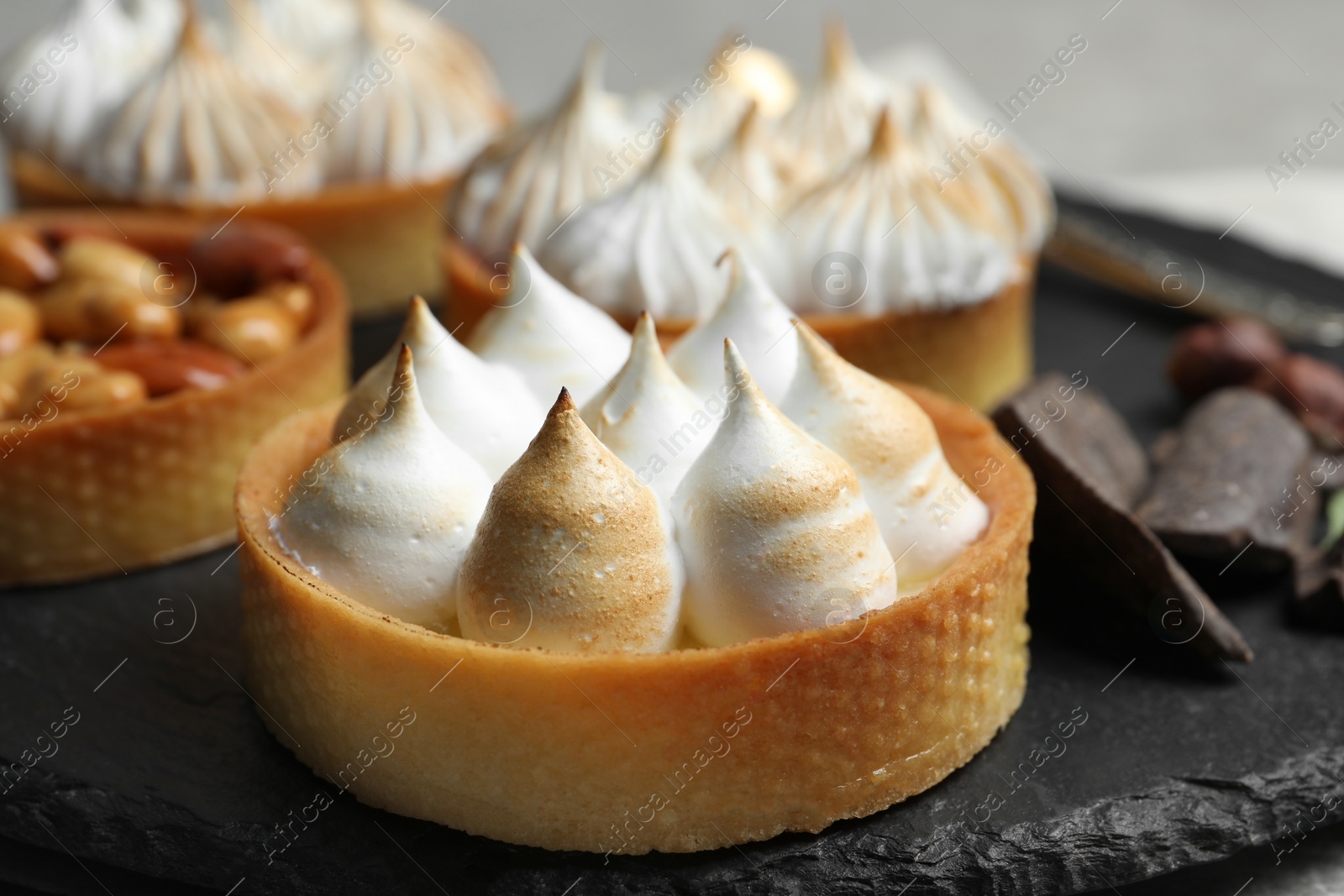 Photo of Different tartlets on black slate, closeup. Delicious dessert