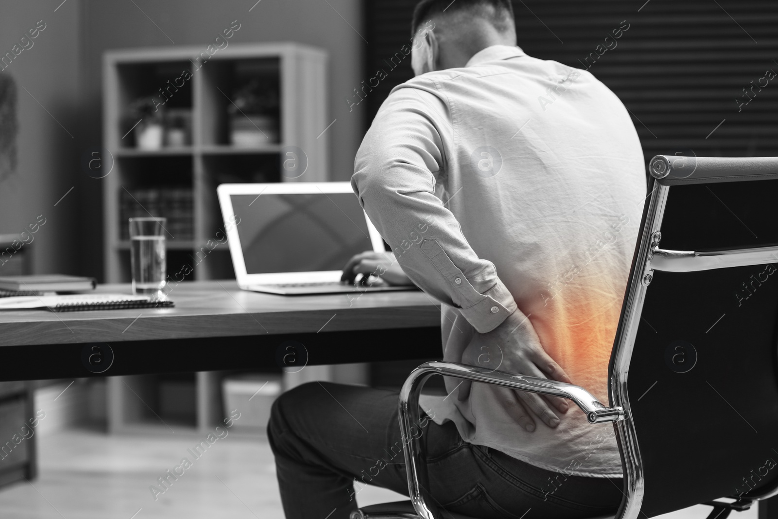 Image of Man suffering from back pain while working with laptop in office. Symptom of poor posture