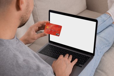 Man with credit card using laptop for online shopping on sofa, closeup