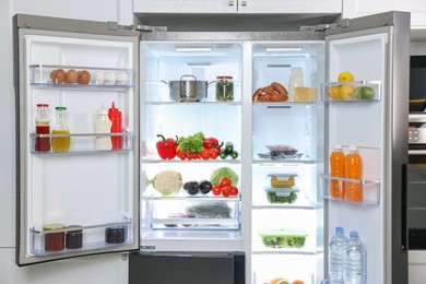 Photo of Modern open refrigerator full of different products in kitchen
