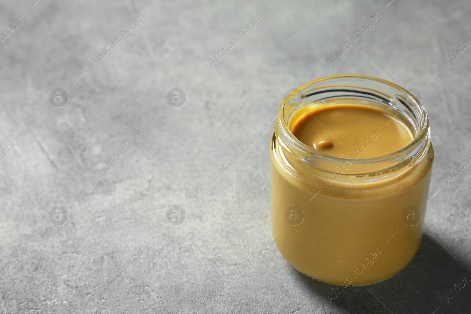 Photo of Spicy mustard in glass jar on grey table. Space for text