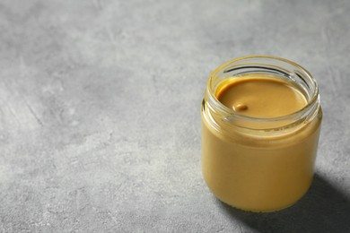 Photo of Spicy mustard in glass jar on grey table. Space for text