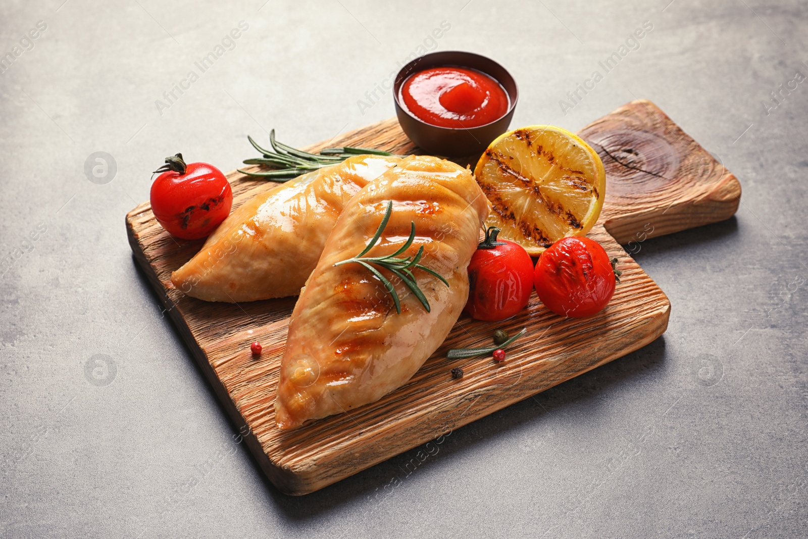 Photo of Wooden board with tasty grilled chicken breasts and garnish on table