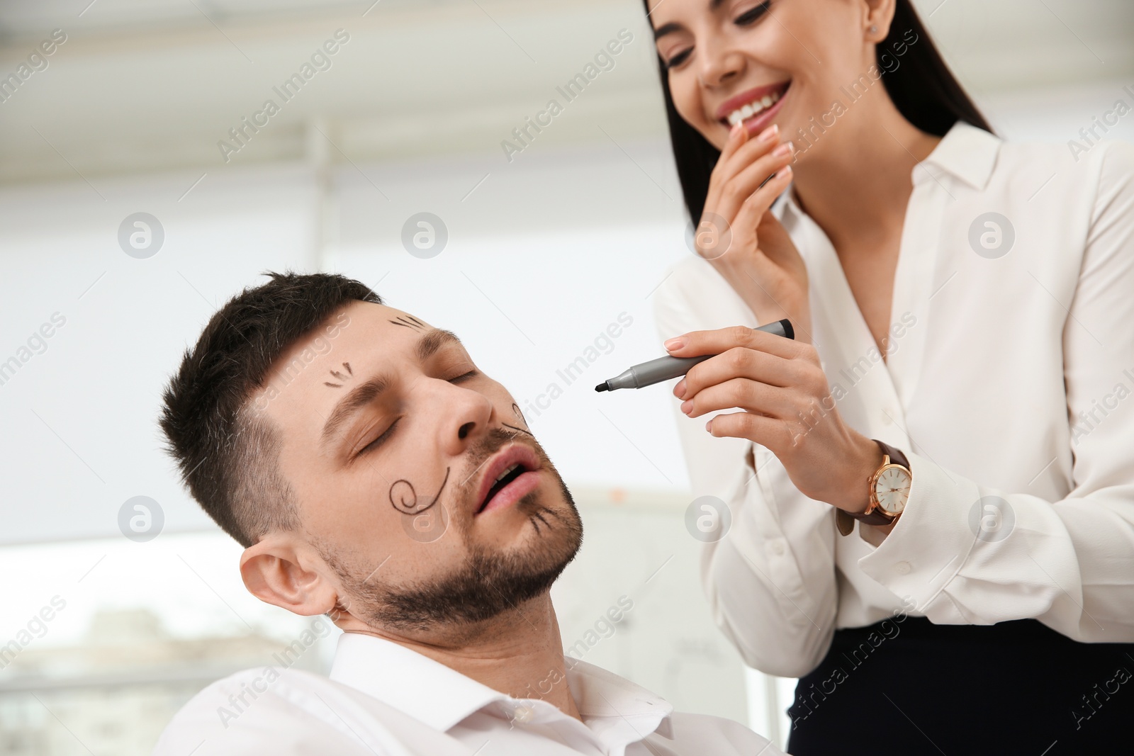 Photo of Young woman drawing on colleague's face while he sleeping in office. Funny joke