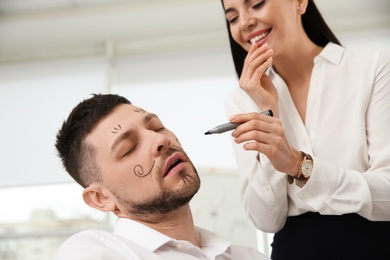 Photo of Young woman drawing on colleague's face while he sleeping in office. Funny joke