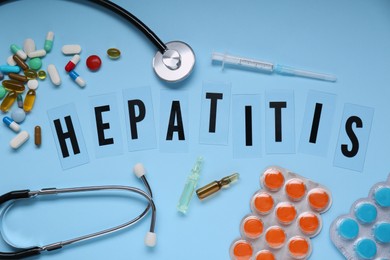 Photo of Word Hepatitis and medical supplies on light blue background, flat lay