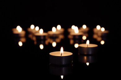 Photo of Burning candle on table against dark background