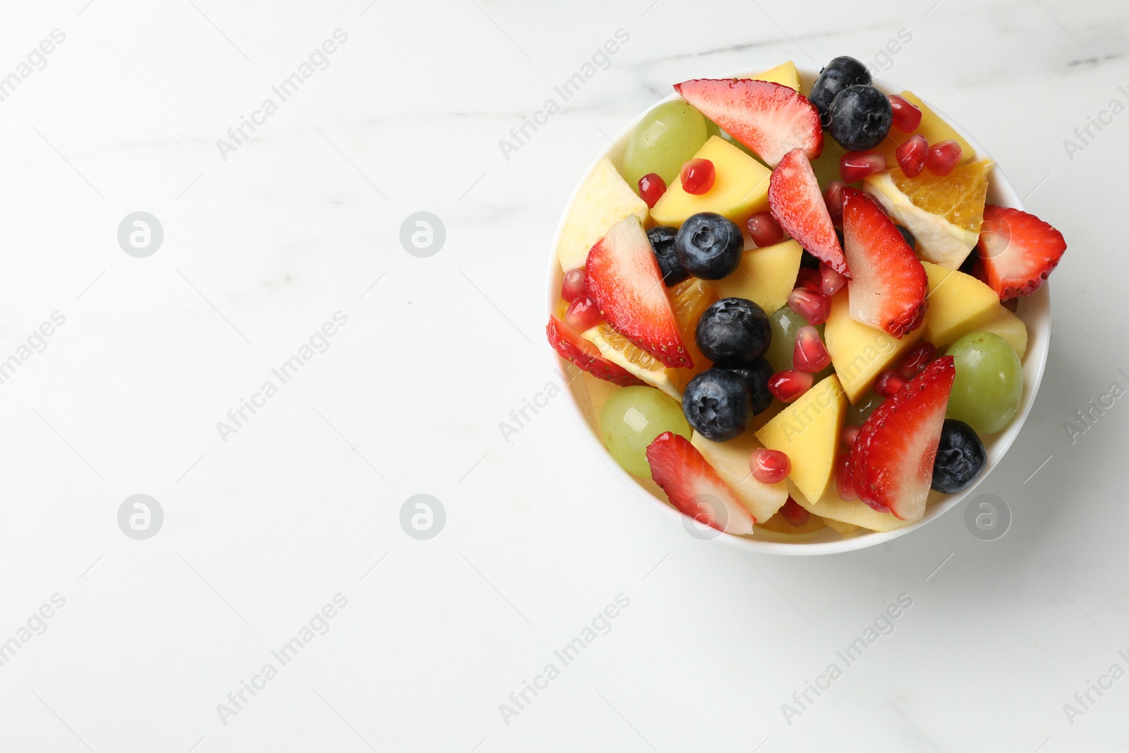 Photo of Tasty fruit salad in bowl on white table, top view. Space for text