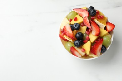 Photo of Tasty fruit salad in bowl on white table, top view. Space for text