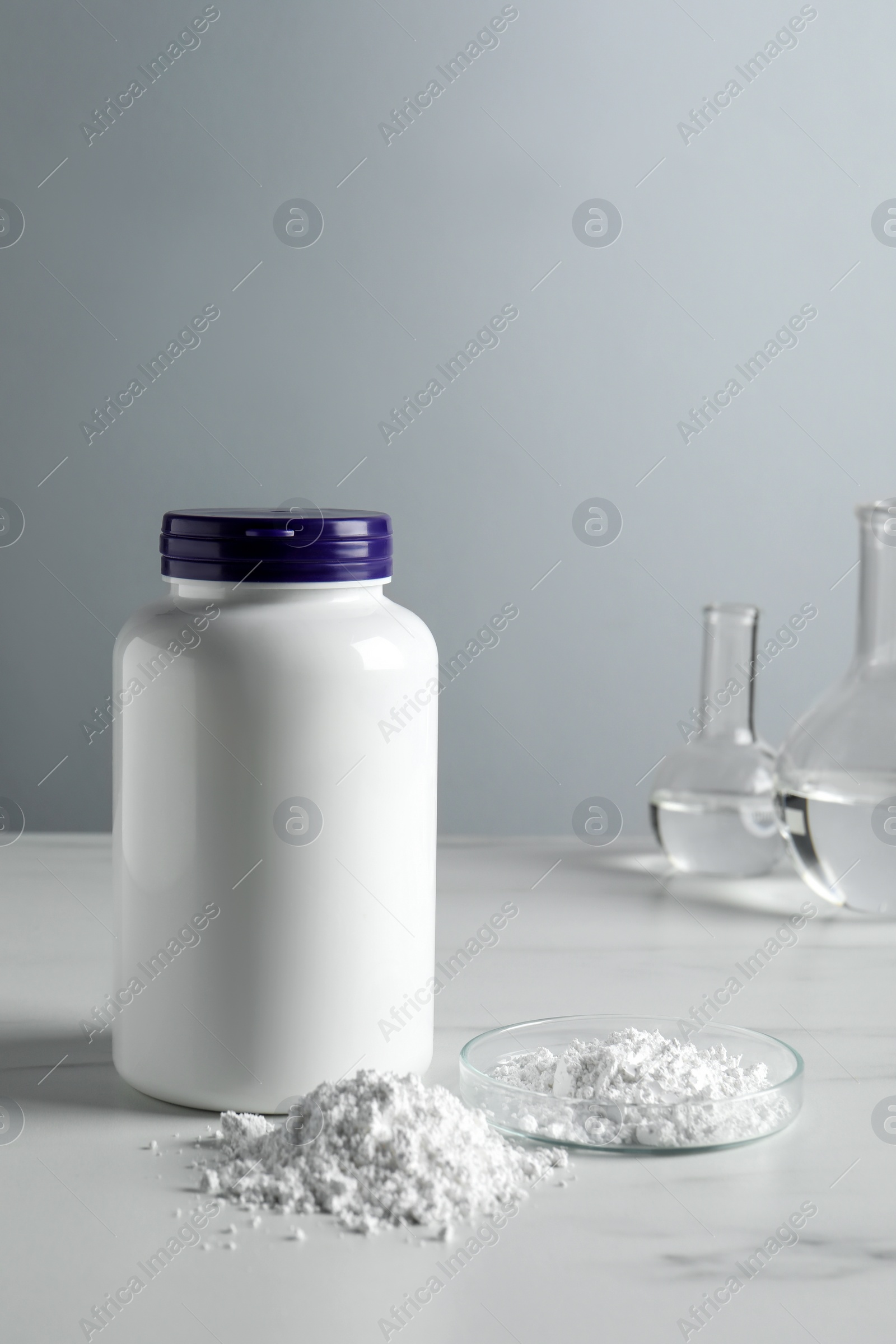 Photo of Calcium carbonate powder, jar and laboratory glassware on white marble table