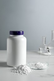 Photo of Calcium carbonate powder, jar and laboratory glassware on white marble table