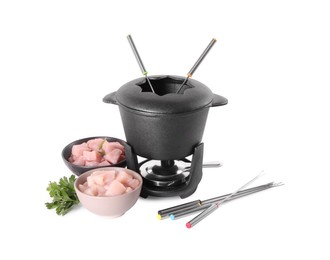 Photo of Fondue pot with oil, forks, raw meat pieces and parsley isolated on white