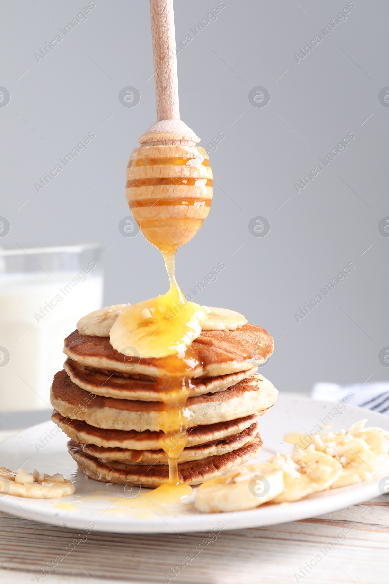 Photo of Pouring honey onto banana pancakes on white wooden table