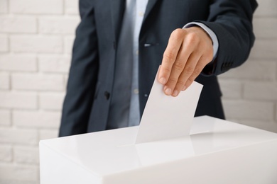 Photo of Man putting his vote into ballot box against brick wall, closeup