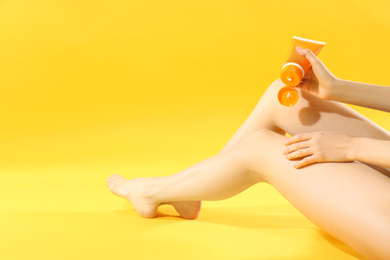 Woman applying sun protection cream on leg against yellow background, closeup. Space for text