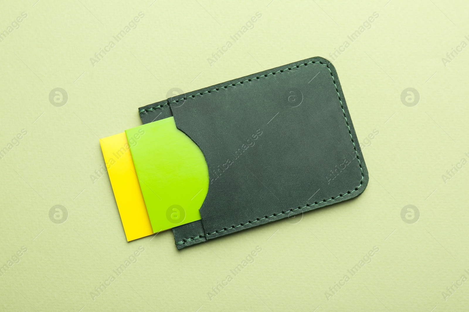 Photo of Leather business card holder with colorful cards on light green background, top view