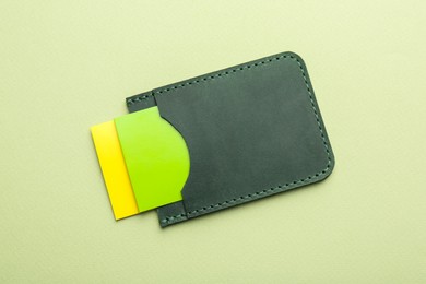 Photo of Leather business card holder with colorful cards on light green background, top view