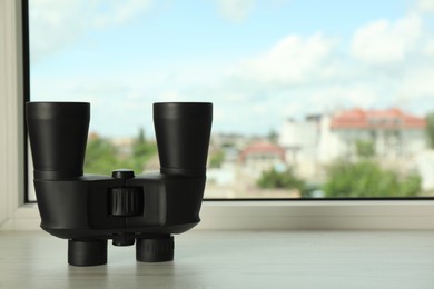 Photo of Black binoculars on white wooden window sill. Space for text