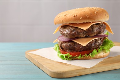 Photo of Tasty hamburger with patties, cheese and vegetables on light blue wooden table, space for text