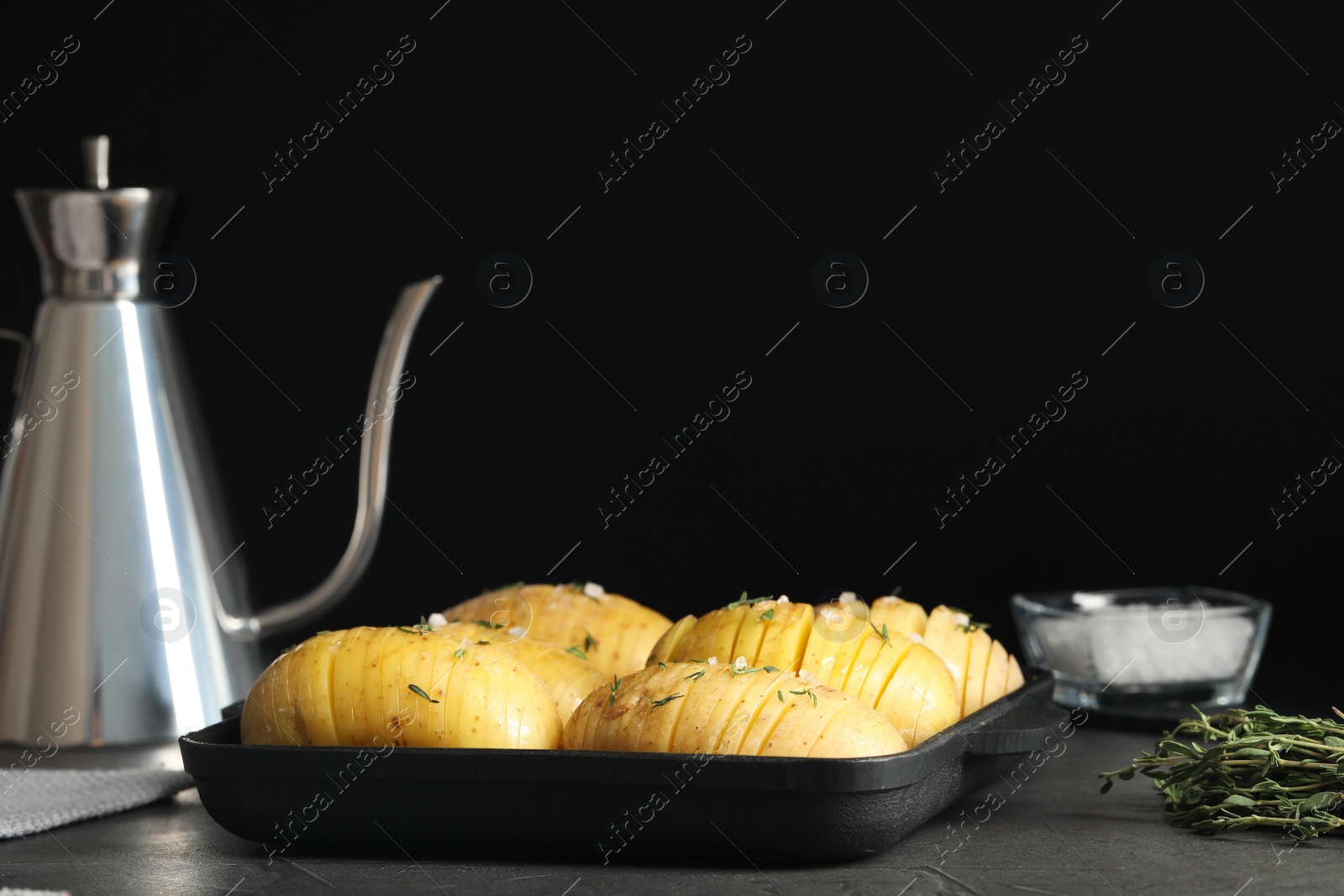 Photo of Raw Hasselback potatoes in baking pan on dark grey table, space for text