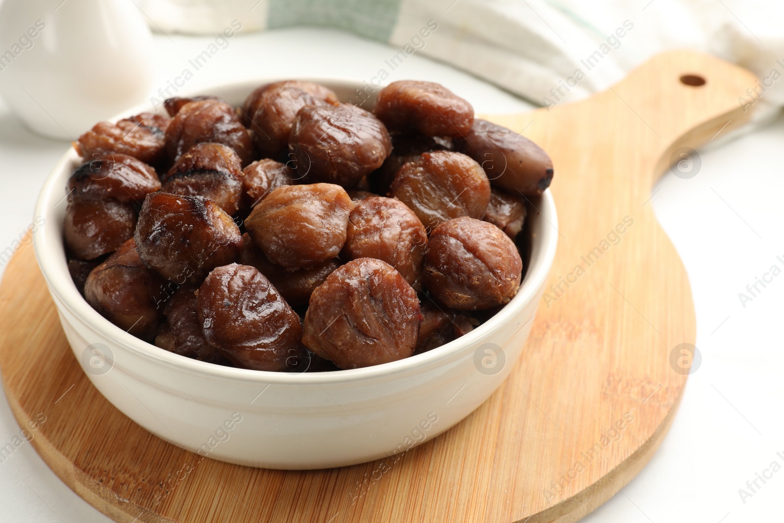 Photo of Roasted edible sweet chestnuts in bowl on white table, closeup