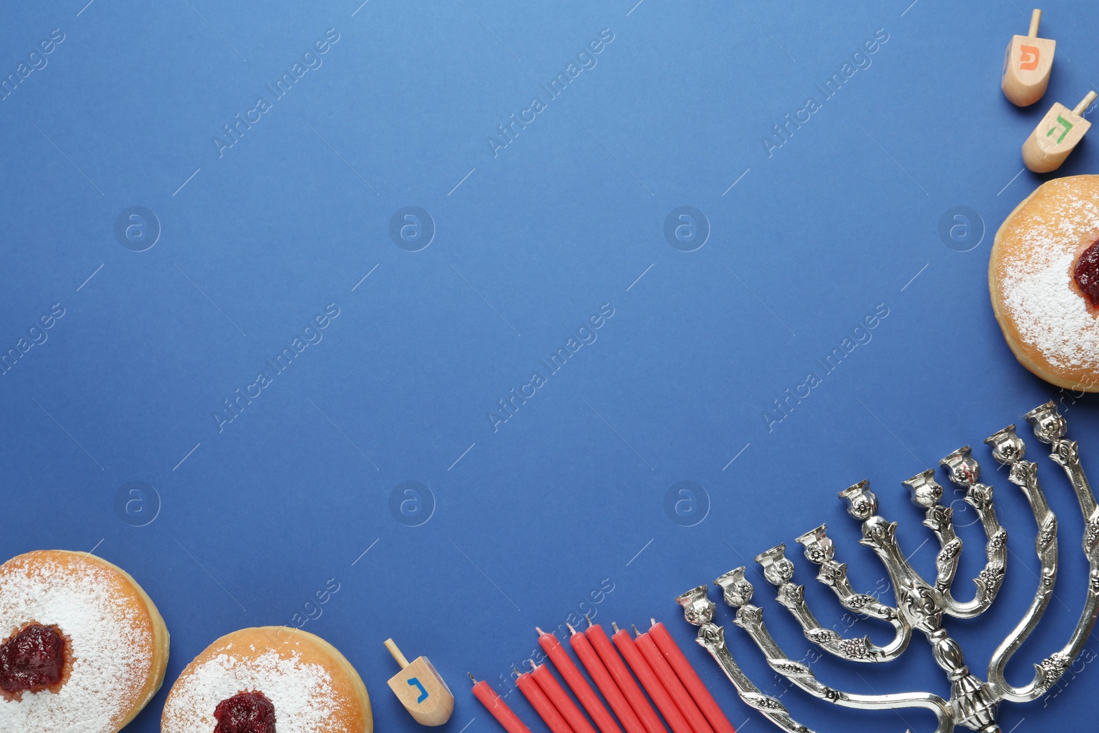 Photo of Hanukkah traditional menorah, candles, doughnuts, dreidels with letters He, Pe, Nun, Gimel on blue background, flat lay. Space for text