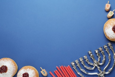 Hanukkah traditional menorah, candles, doughnuts, dreidels with letters He, Pe, Nun, Gimel on blue background, flat lay. Space for text