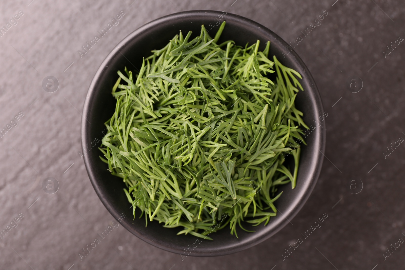 Photo of Fresh cut dill in bowl on dark table, top view