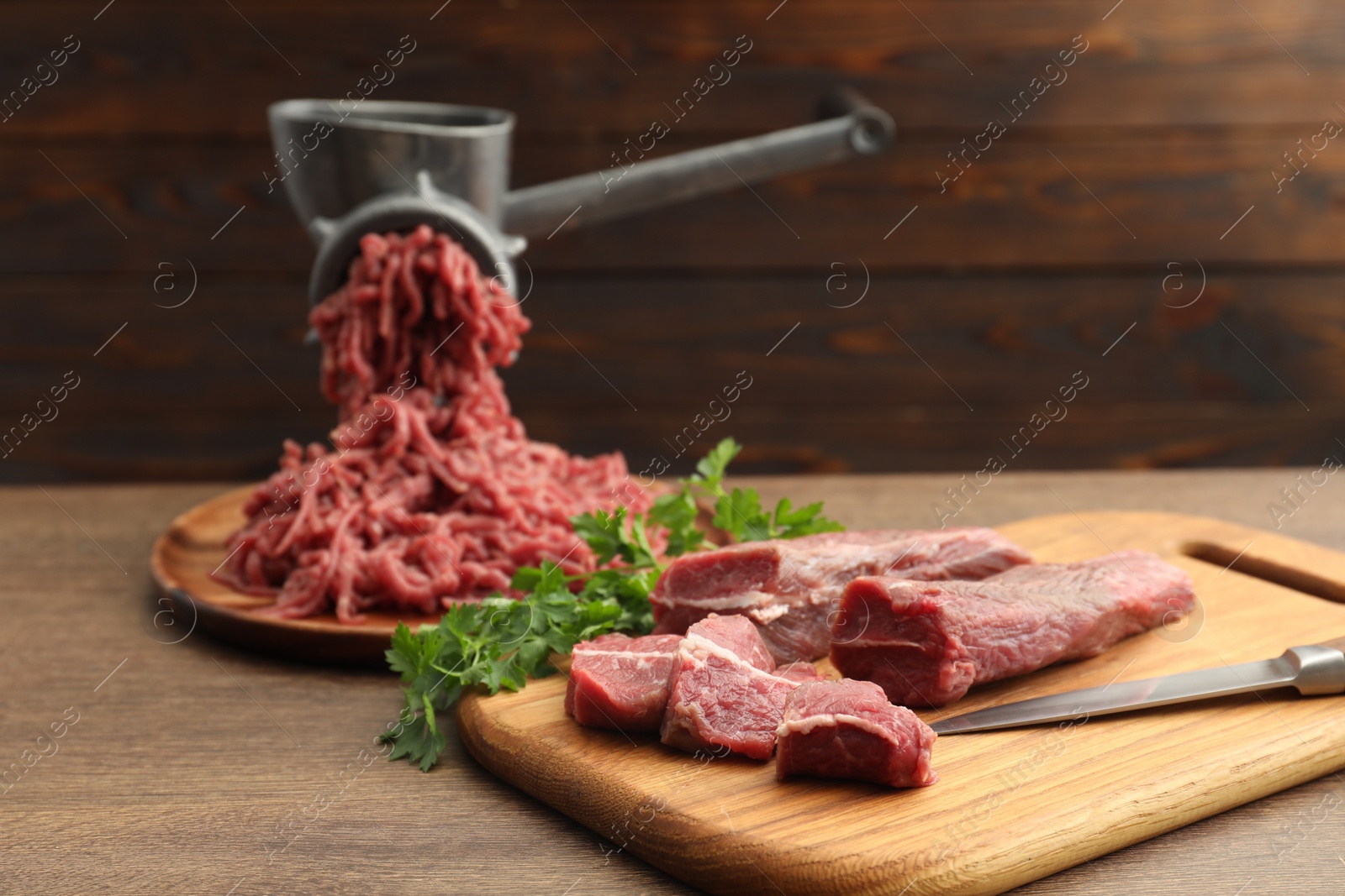 Photo of Manual meat grinder with beef and parsley on wooden table