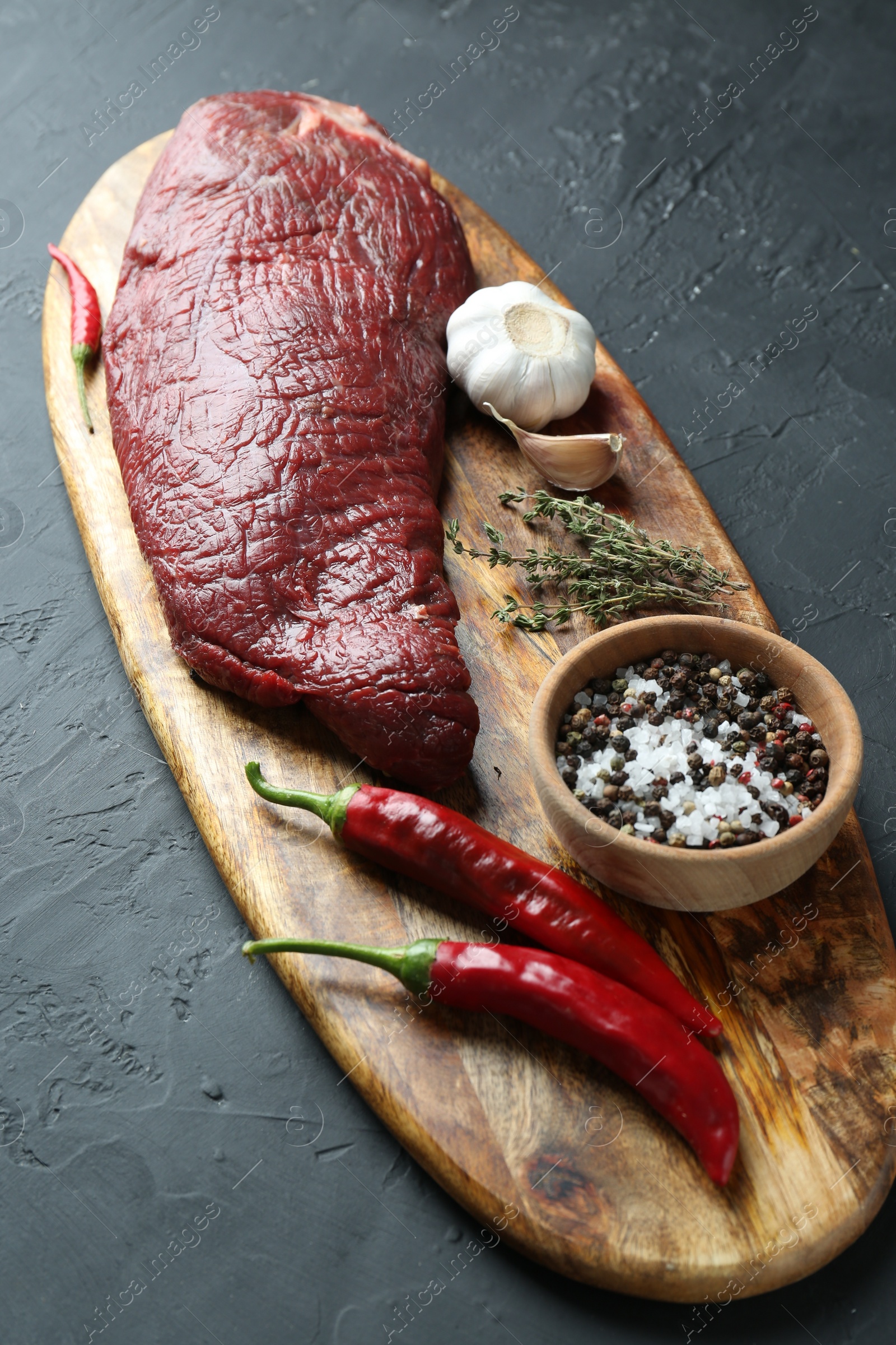 Photo of Piece of raw beef meat, products and spices on dark grey textured table