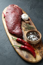 Piece of raw beef meat, products and spices on dark grey textured table