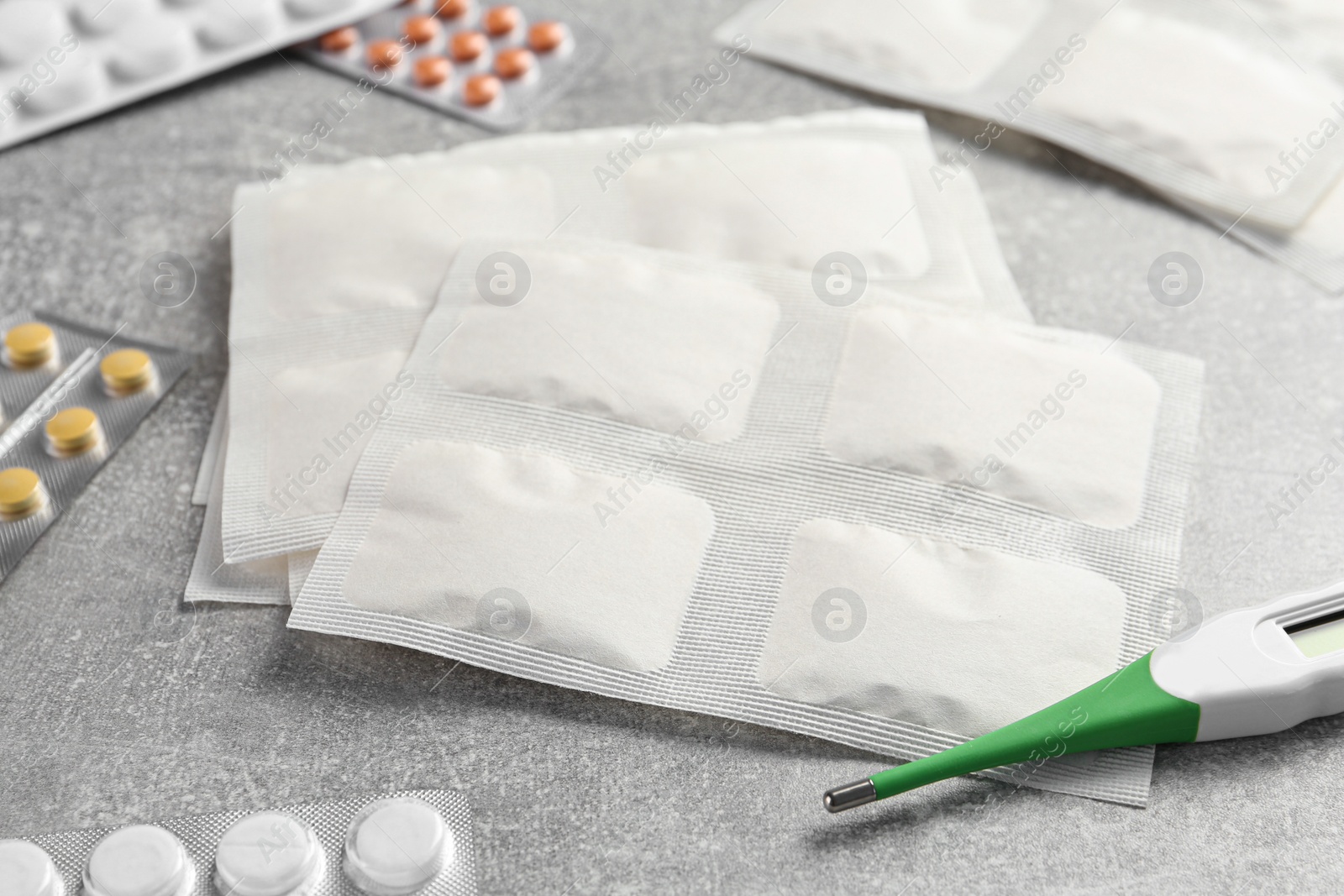 Photo of Mustard plasters, pills and thermometer on light grey table, closeup