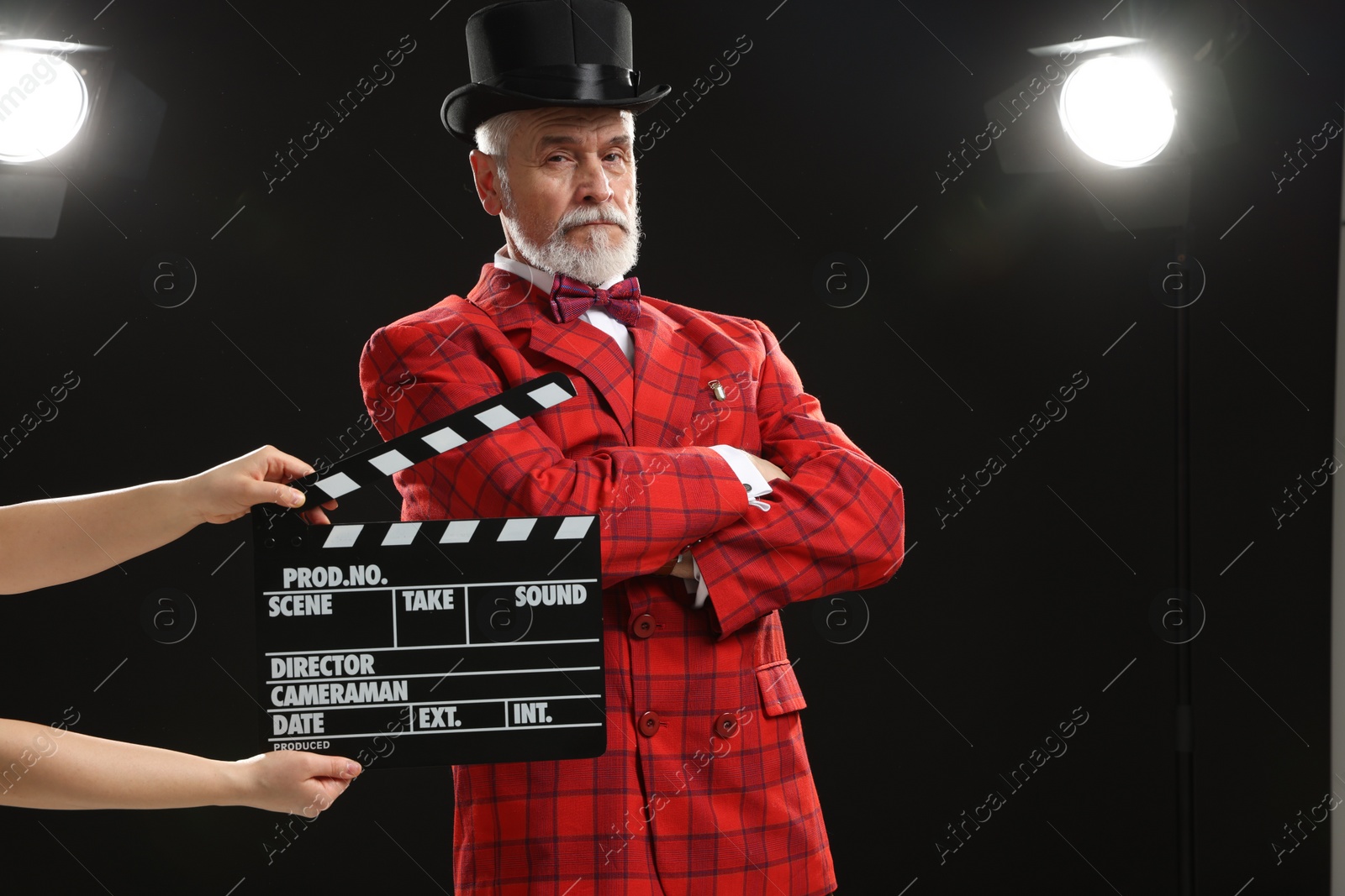 Photo of Senior actor performing role while second assistant camera holding clapperboard on stage. Film industry