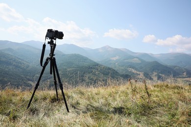 Photo of Tripod with modern camera in mountains on sunny day. Professional photography