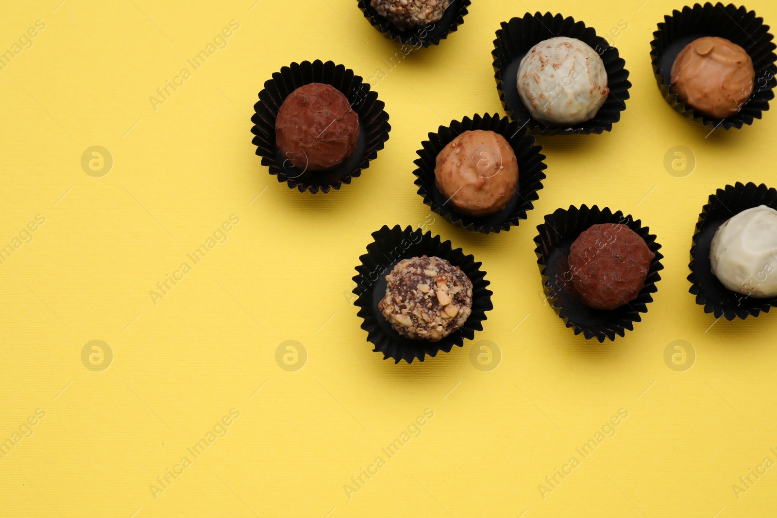 Photo of Different tasty chocolate candies on yellow background, flat lay. Space for text