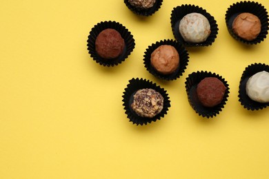 Different tasty chocolate candies on yellow background, flat lay. Space for text