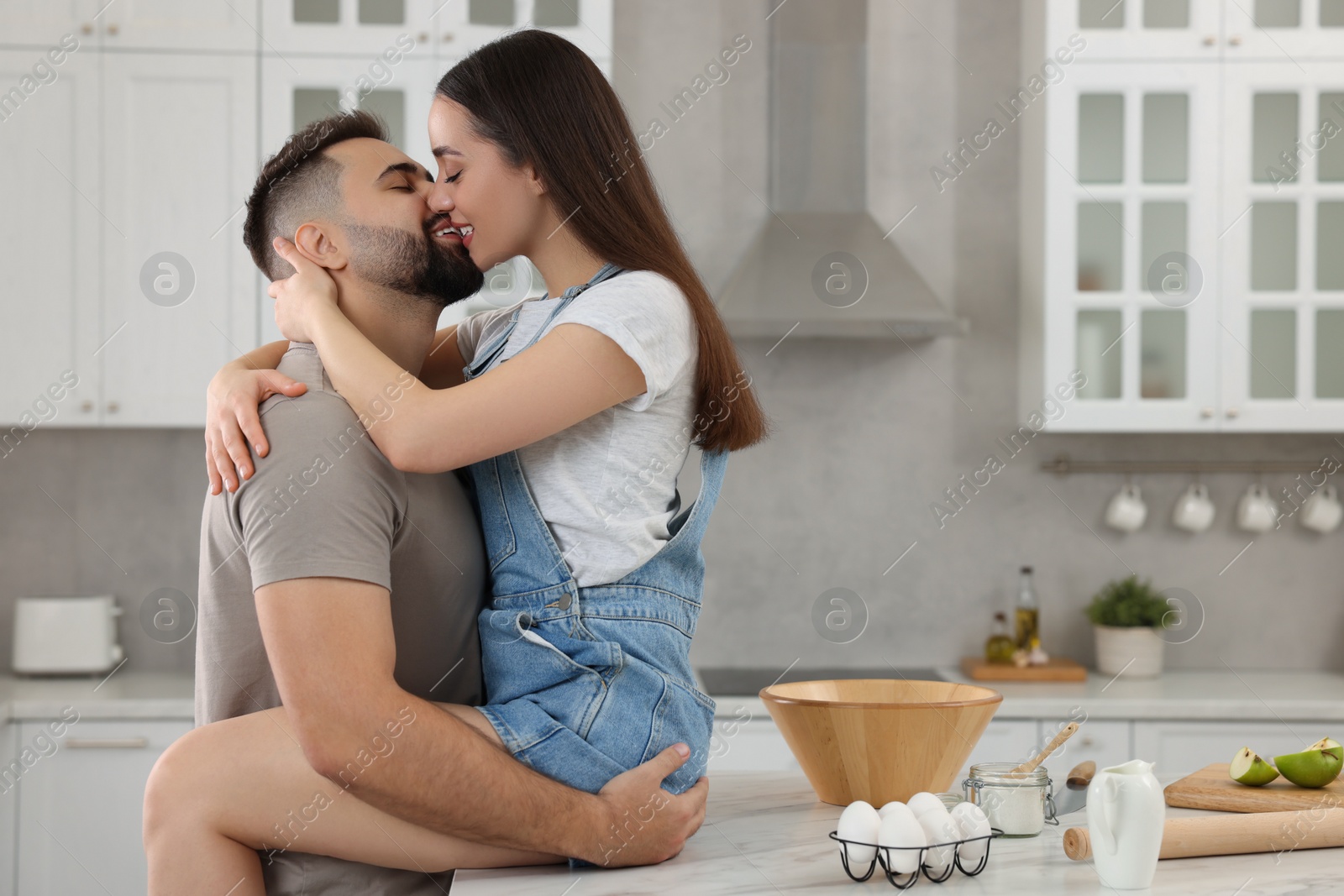 Photo of Affectionate young couple kissing in kitchen. Space for text