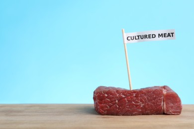 Photo of Sample of lab grown beef labeled Cultured Meat on wooden table. Space for text