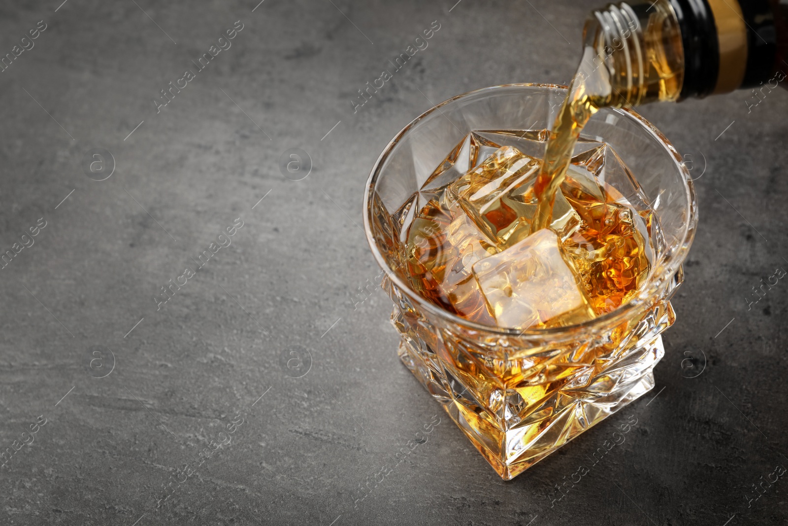 Photo of Pouring whiskey from bottle into glass with ice cubes on table. Space for text