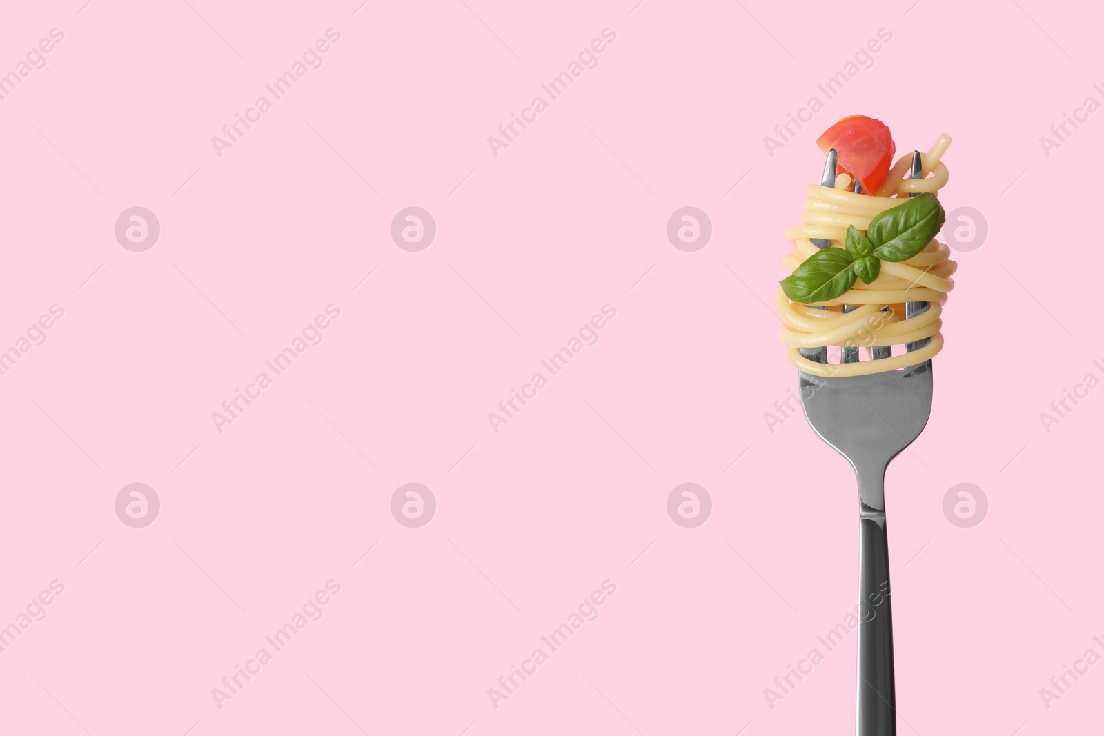 Photo of Fork with tasty pasta, piece of fresh tomato and basil on pink background, space for text