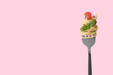 Photo of Fork with tasty pasta, piece of fresh tomato and basil on pink background, space for text