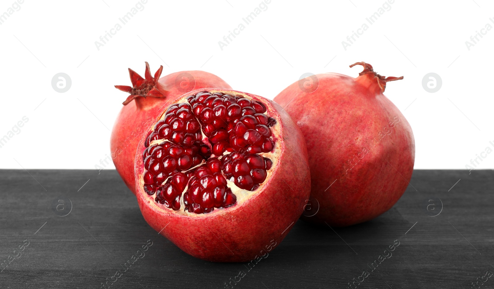 Photo of Fresh pomegranates on black wooden table against white background