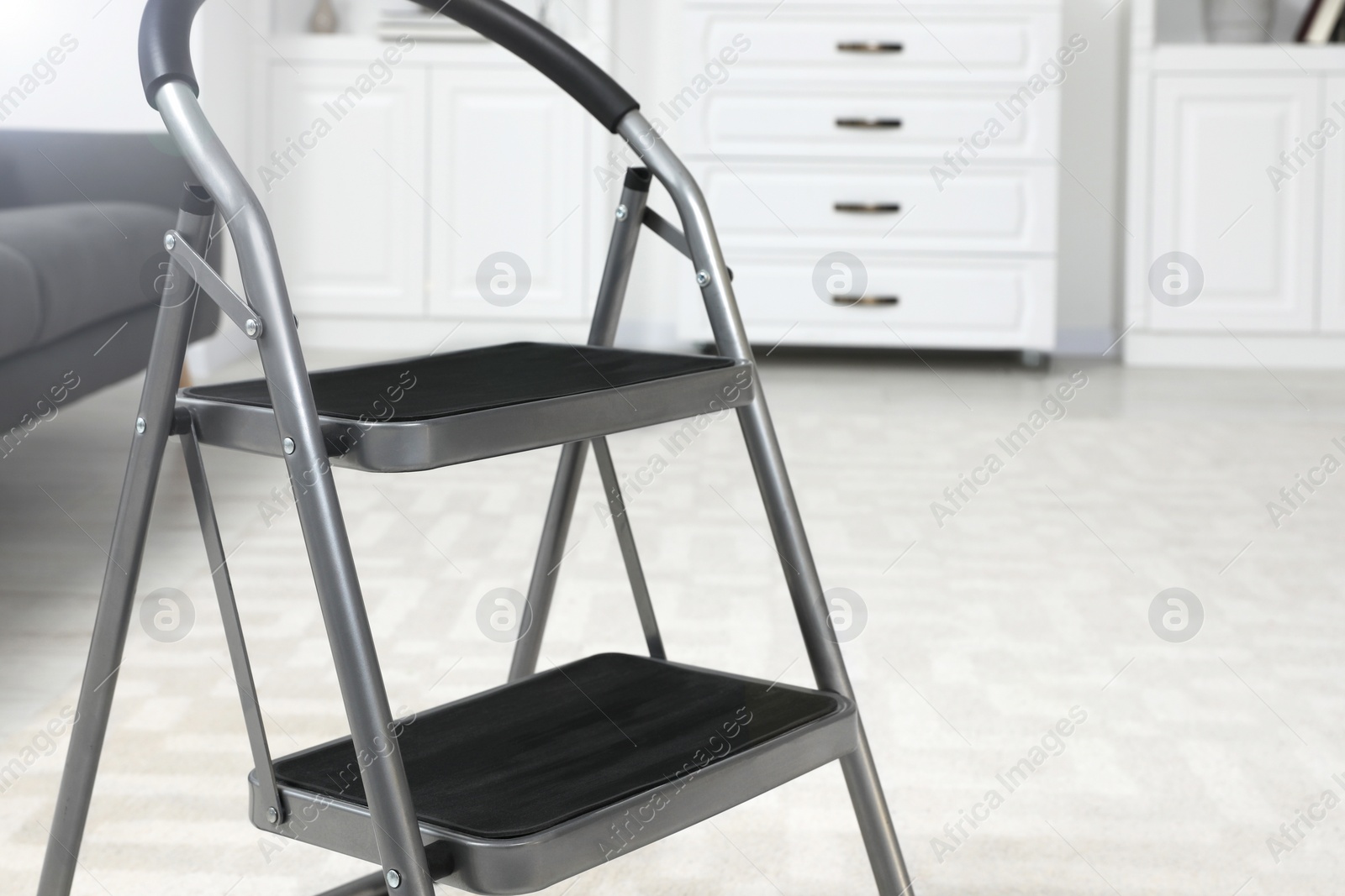 Photo of Metal folding ladder on soft carpet in room