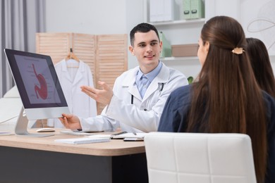 Gastroenterologist consulting woman with her daughter and showing image of stomach on computer in clinic