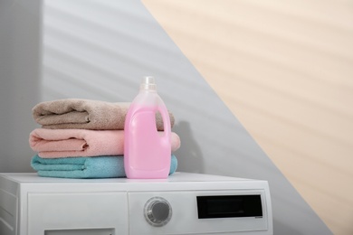 Photo of Bottle of laundry detergent and clean towels on washing machine indoors, space for text