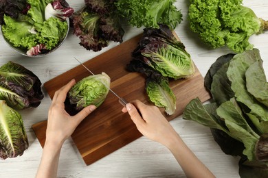 Photo of Woman cutting red romaine lettuce at white wooden table, top view