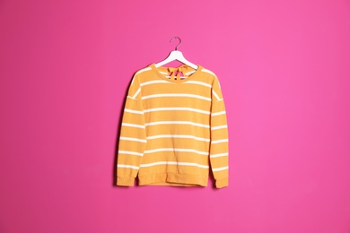 Hanger with stylish sweater on color background