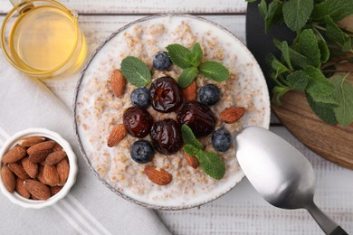 Photo of Tasty wheat porridge with milk, dates, blueberries and almonds in bowl served on table, flat lay