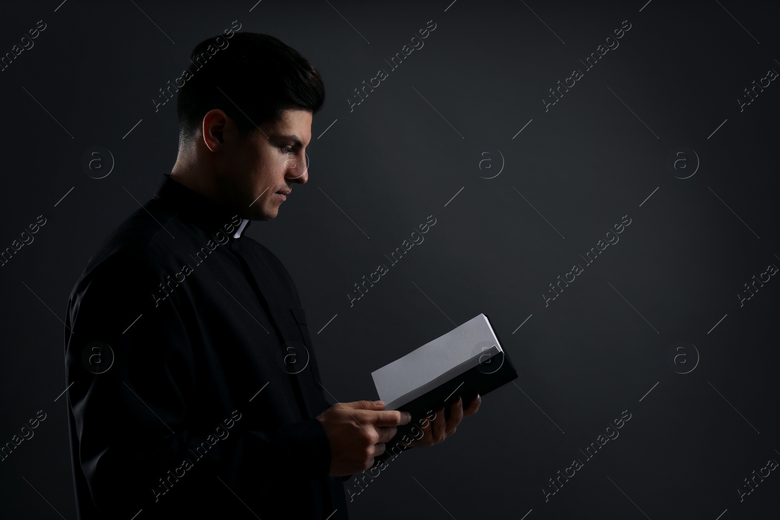 Photo of Priest with Bible on black background. Space for text