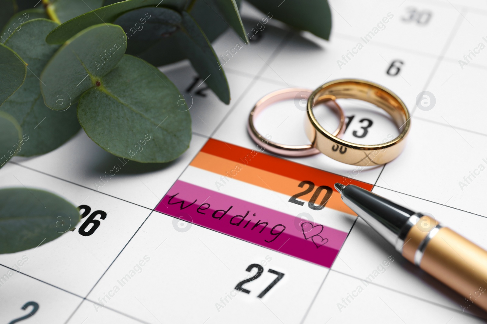 Image of Calendar with date reminder in color of lesbian flag about Wedding Day, pen and rings, closeup